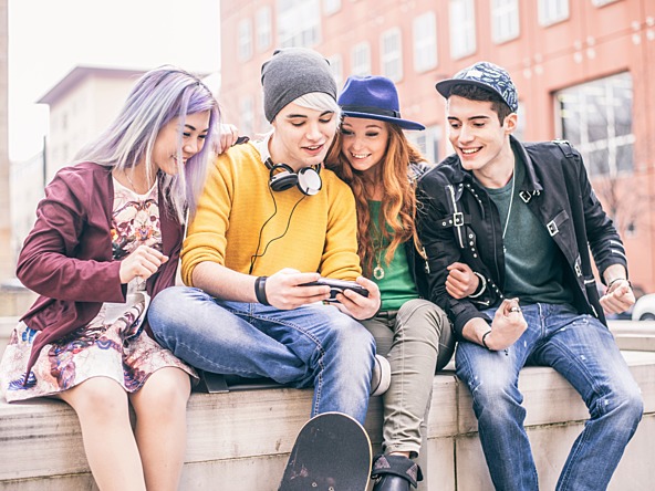 Group of teenagers sit on a wall and look at a phone